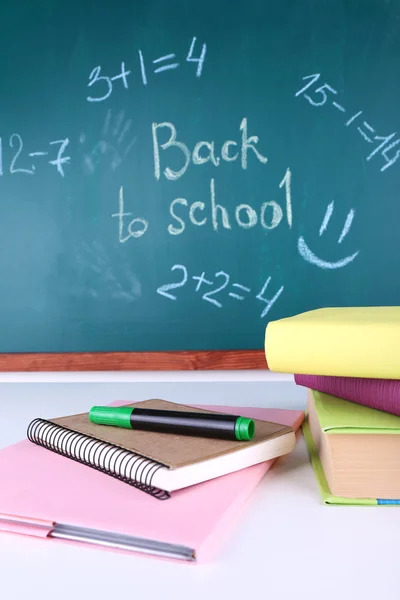 School supplies on table on blackboard background — Stock Photo, Image