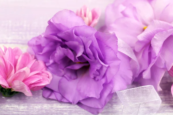 Beautiful chrysanthemum and artificial eustoma flowers on purple wooden background — Stock Photo, Image