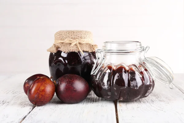 Mermelada de ciruela y ciruelas frescas en plato de vidrio sobre mesa de madera sobre fondo claro —  Fotos de Stock