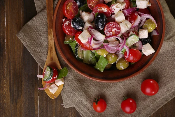 Greek salad served in brown bowl on sacking napkin on wooden background — Stock Photo, Image
