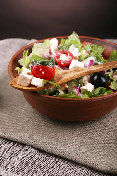 Bowl of Greek salad served on napkin on wooden table on dark background — Stock Photo, Image