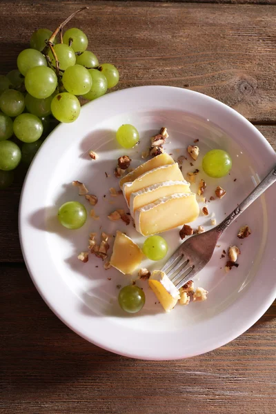 Tasty grape and cheese on plate, on wooden table — Stock Photo, Image