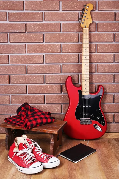 Guitarra, treinadores e roupas no fundo da parede de tijolo — Fotografia de Stock