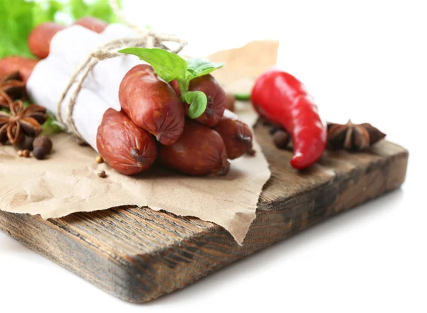 Salsicce sottili affumicate con foglie di insalata di lattuga e spezie su tagliere di legno, isolate su bianco — Foto Stock