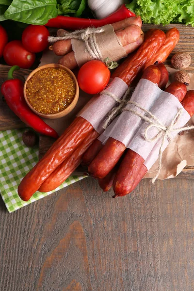 Assortment of thin sausages, mustard in bowl and spices on cutting board, on wooden background — Stock Photo, Image