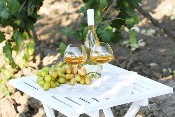 Uva madura, garrafa de vinho e taças na mesa de madeira no fundo do arbusto de uva — Fotografia de Stock