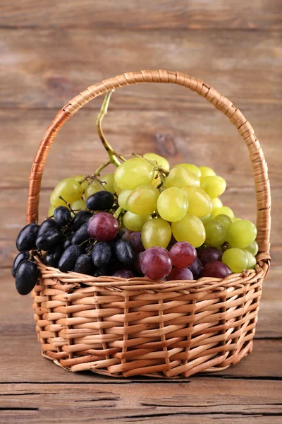 Diferentes tipos de uvas em cesta de vime no fundo de madeira — Fotografia de Stock