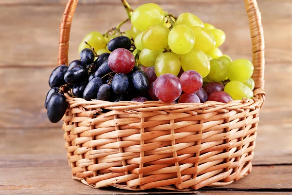 Diferentes tipos de uvas em cesta de vime no fundo de madeira — Fotografia de Stock