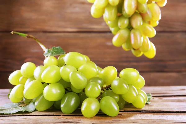 Bunches of ripe grapes on wooden table on wooden wall background — Stock Photo, Image