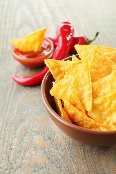 Nachos saborosos, tomates vermelhos e pimenta na tigela de cor no fundo de madeira — Fotografia de Stock