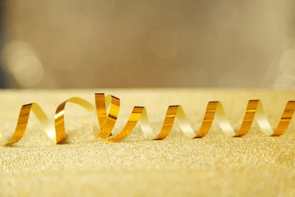 Fita de serpentina na mesa em fundo dourado brilhante — Fotografia de Stock