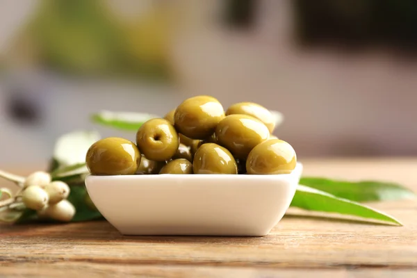 Olive verdi in ciotola con foglie sul tavolo su fondo chiaro — Foto Stock