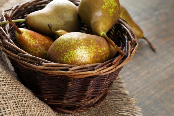 Rijpe peren in rieten mand, op houten achtergrond — Stockfoto