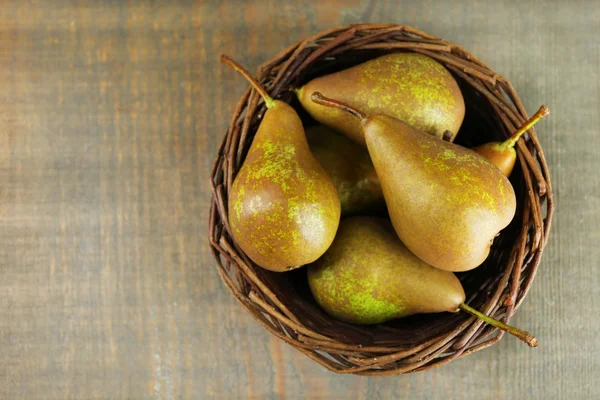 Rijpe peren in rieten mand, op houten achtergrond — Stockfoto