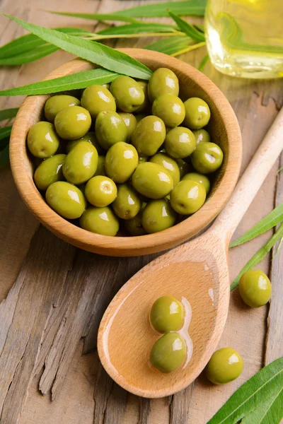 Groene olijven in kom met bladeren op tabel close-up — Stockfoto