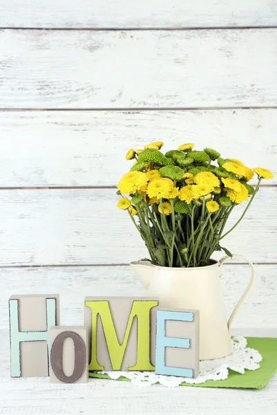 Yellow and green flowers in decorative jug on color wooden background — Stock Photo, Image