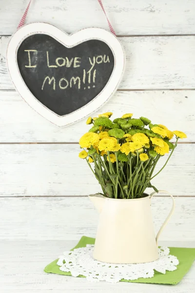 Gele en groene bloemen in decoratieve kruik op een houten achtergrond kleur — Stockfoto