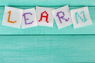 ahşap zemin üzerinde beyaz kumaş üzerine işlemeli harflerden kelime yapılmış