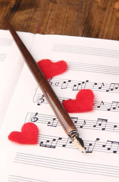 Red paper hearts on music book, close-up, on wooden background — Stock Photo, Image