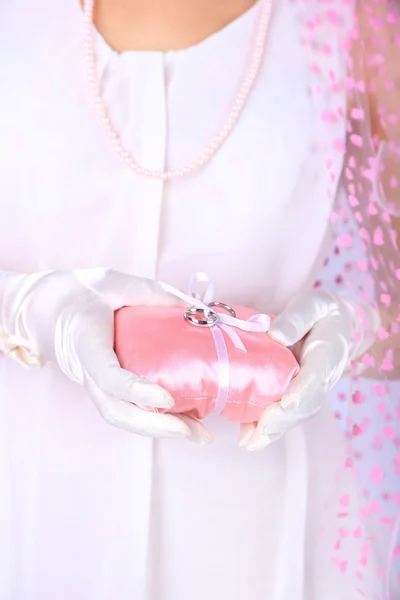 Bride in white dress and gloves holding decorative pillow with wedding rings, close-up — Stock Photo, Image