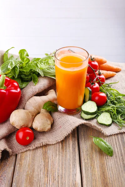 Glass of fresh carrot juice and vegetables on sacking napkin on wooden table — Stock Photo, Image