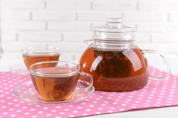 Theepot en kopjes thee op tafel op bakstenen muur achtergrond — Stockfoto