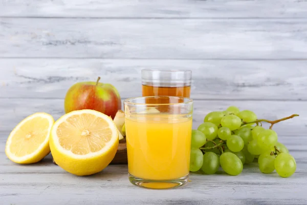 Szklanki soku ze świeżych owoców na szary drewniany stół — Zdjęcie stockowe