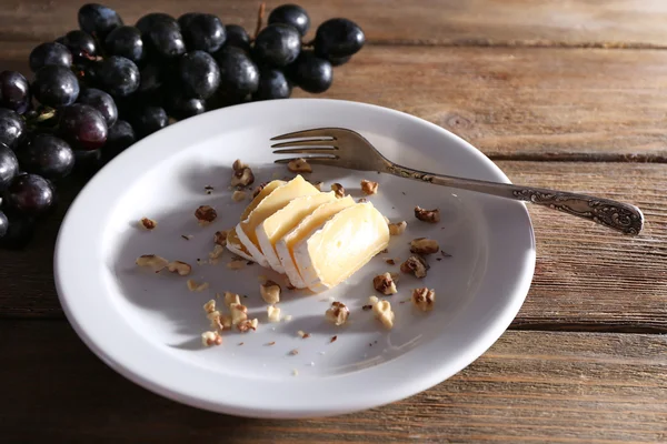 La uva sabrosa y el queso en el plato, sobre la mesa de madera —  Fotos de Stock