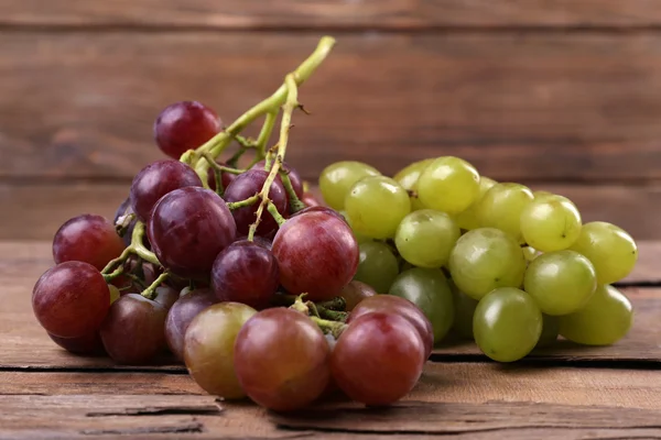 Bunches of different kinds of grapes on wooden table on wooden wall background — Stock Photo, Image