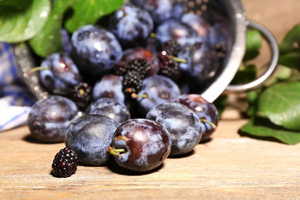 Ripe sweet plums in metal colander, on wooden table — Stock Photo, Image