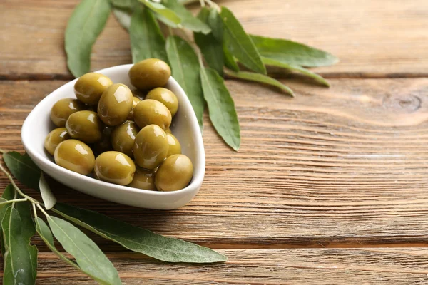 Green olives in bowl with leaves on table close-up — Stock Photo, Image