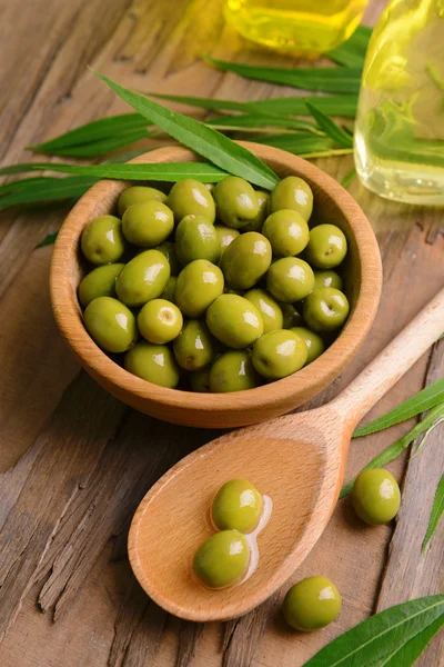 Groene olijven in kom met bladeren op tabel close-up — Stockfoto