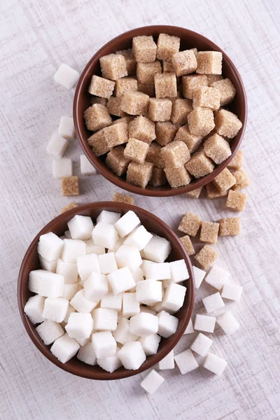 Hnědý a bílý rafinovaný cukr v barevné misky na dřevěné pozadí — Stock fotografie