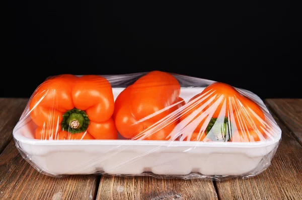 Poivre emballé dans un film alimentaire sur table sur fond noir — Photo