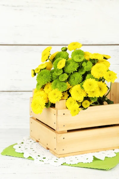 Yellow and green flowers in wooden box, on wooden background