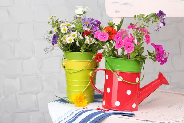 Bouquet of colorful flowers in decorative buckets, on chair, on light wall background — Stock Photo, Image