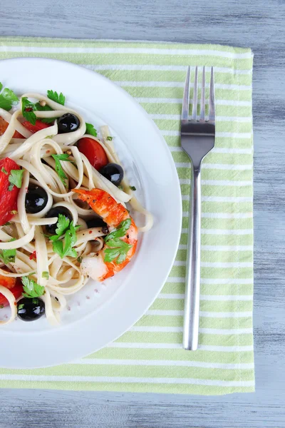 Čerstvé krevety s špagety, olivami, rajčaty a petrželkou v velké kulaté desky na ubrousek na dřevěné pozadí — Stock fotografie