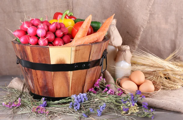 Big round basket with dried grass, vegetables, milk and fresh eggs on sacking background — Stock Photo, Image