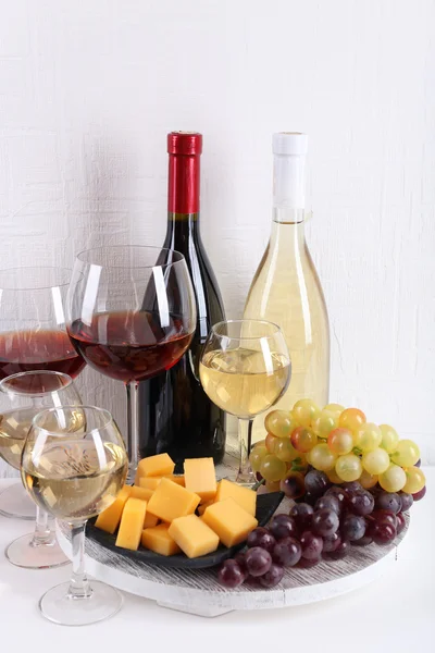 Bottles and glasses of wine, cheese and ripe grapes on table in room — Stock Photo, Image