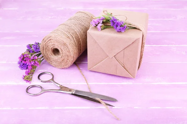 Beautiful gift with flowers and decorative rope, on old wooden background — Stock Photo, Image