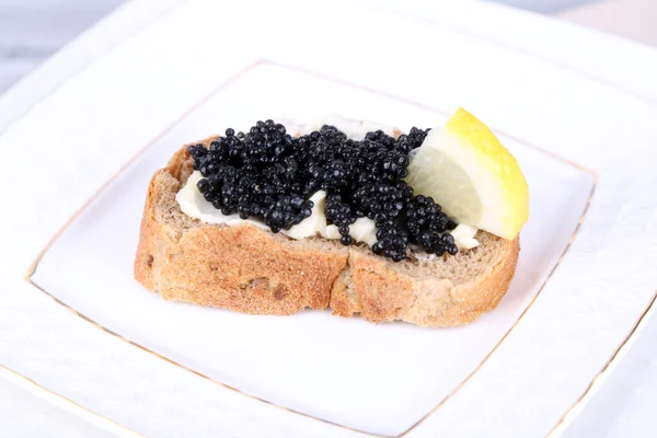 Rebanada de pan con mantequilla, caviar negro y limón en el plato —  Fotos de Stock