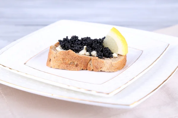 Tranche de pain au beurre, caviar noir et citron sur fond gris — Photo