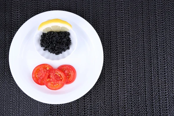 Caviar preto com fatias de tomate na placa no fundo de tecido escuro — Fotografia de Stock