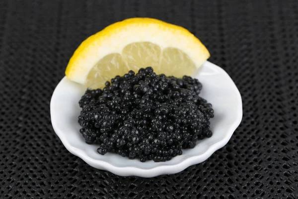 Caviale nero con limone su piatto su sfondo tessuto scuro — Foto Stock