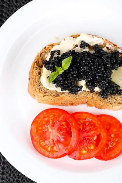 Caviar negro y mantequilla en pan con tomates en plato sobre fondo de tela oscura —  Fotos de Stock