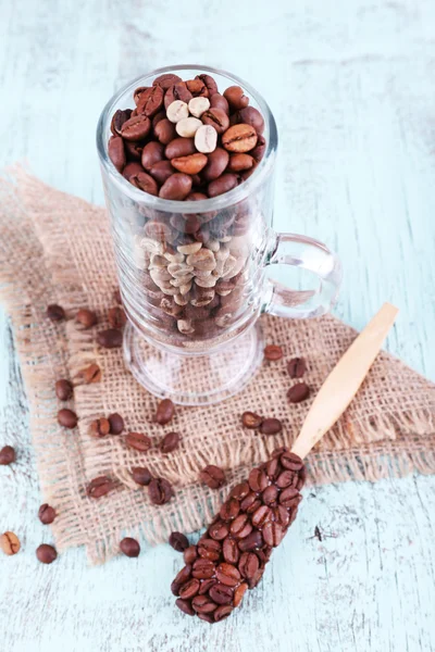 Bicchiere e cucchiaio con chicchi di caffè su sacco su sfondo di legno blu — Foto Stock