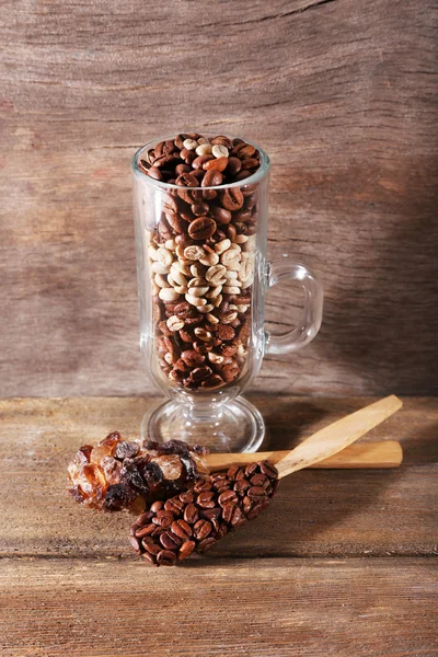 Glass and spoons with coffee beans on wooden table on wooden background — Stock Photo, Image