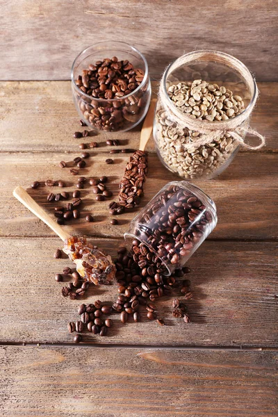 Pots en verre et cuillère avec grains de café sur fond en bois — Photo