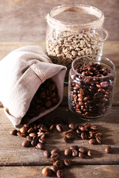Coffee beans in fabric bag and glass jars on wooden table on wooden background — Stock Photo, Image