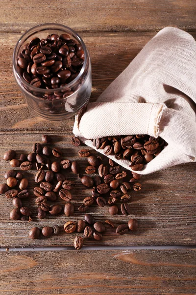 Kávová zrna v látkové vaky a skleněná dóza na dřevěné pozadí — Stock fotografie